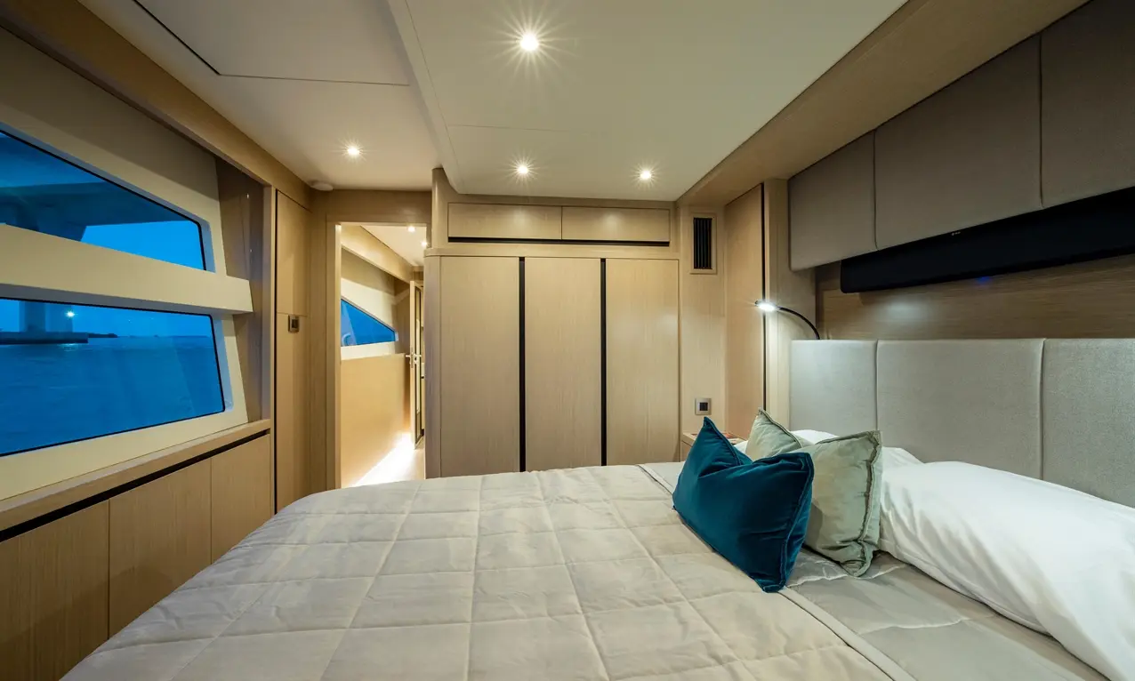 Luxurious yacht cabin with a double bed, decorative cushions, wooden finishes, and large windows showcasing a scenic view.